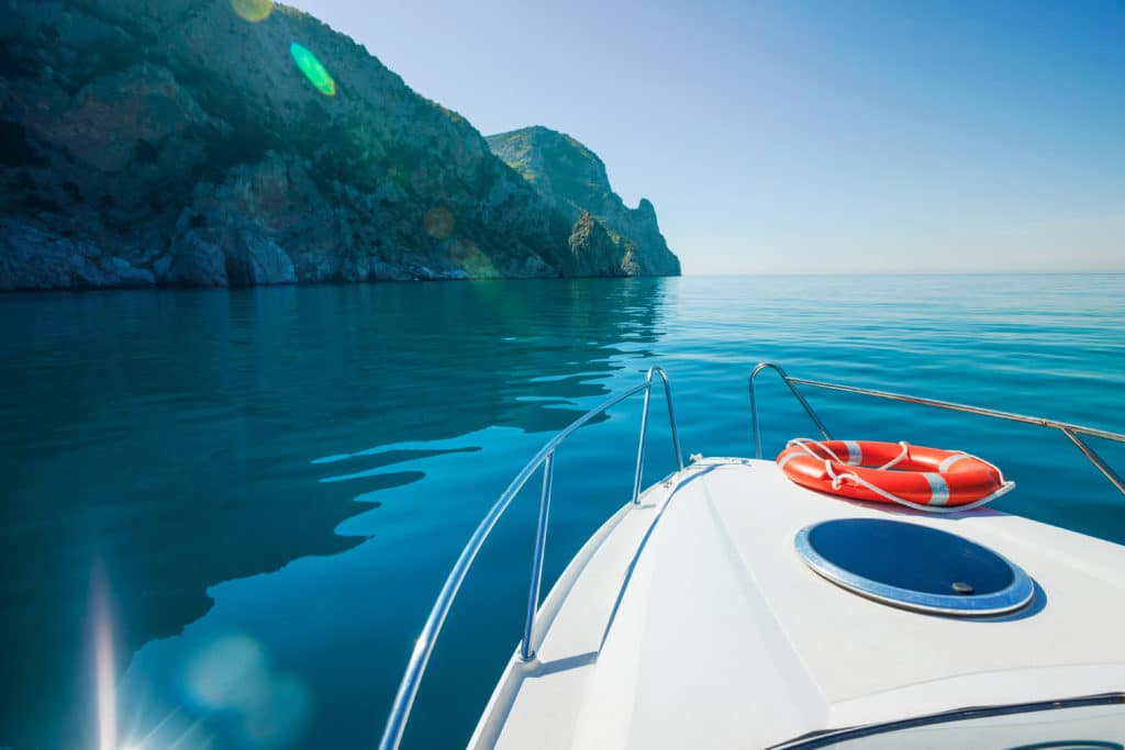 A boat on still, blue water near a cliff covered in greenery.