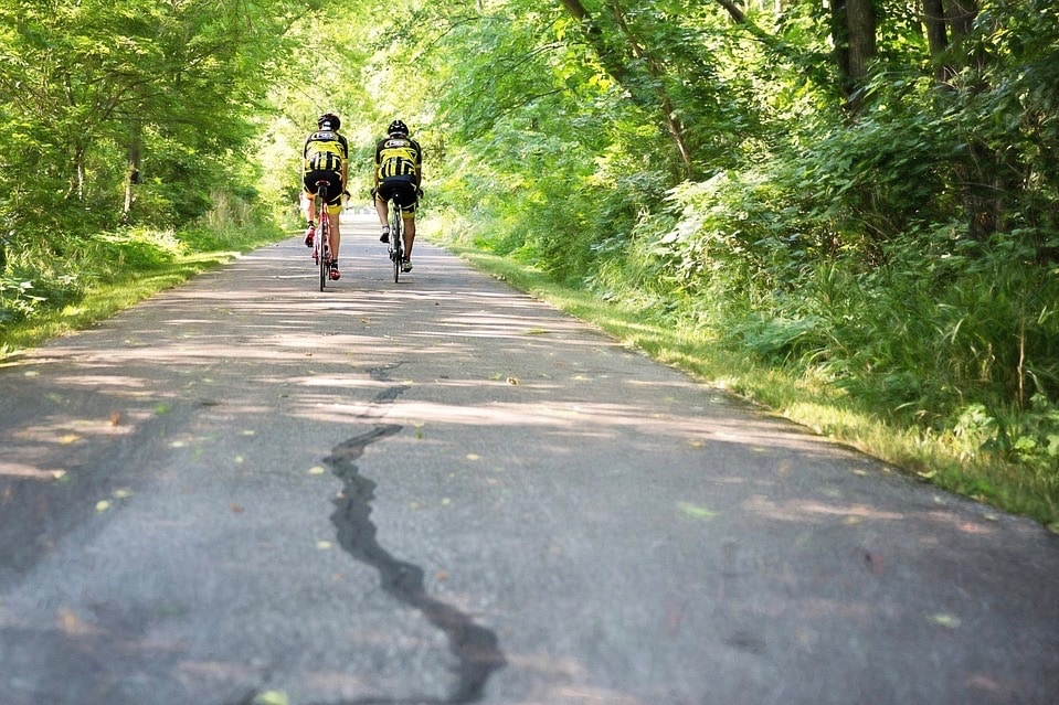 Two bikers riding down a bike path in the summer.
