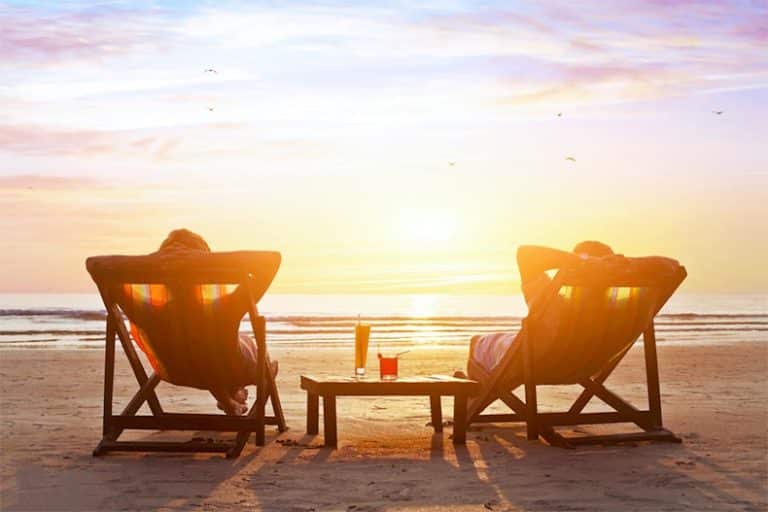 Two 55+ active adults relaxing in lounge chairs by the beach.