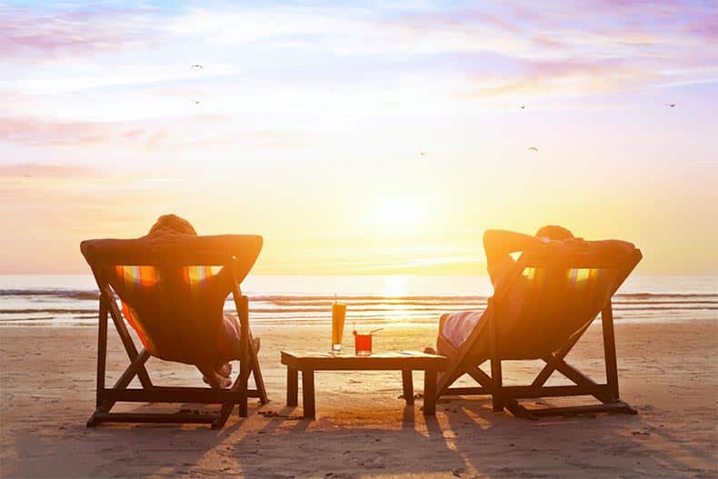 Two 55+ active adults relaxing in lounge chairs by the beach.