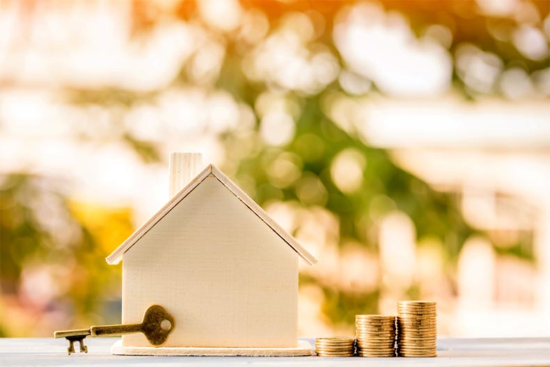 A key and a stack of coins beside a wooden house model.