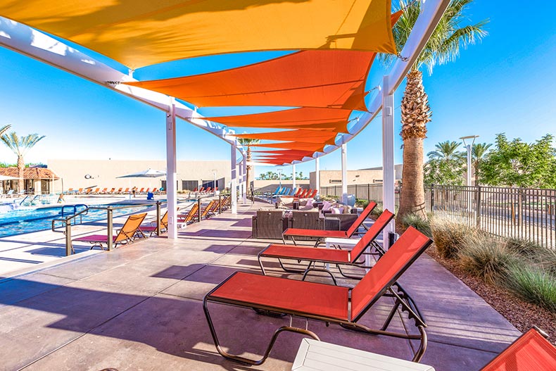 Pool and pool deck with orange lounge chairs underneath yellow and orange sail canopies.