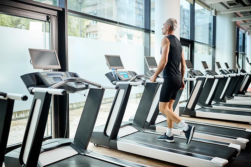 An older man exercising on a treadmill in the fitness center at his 55+ community.