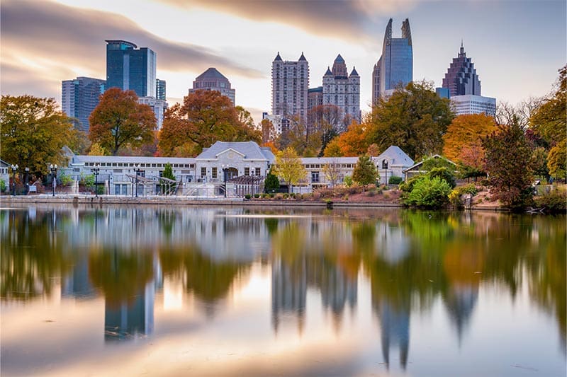 Evening view of Atlanta skyline during autumn with a lake and autumn leaves in the foreground.