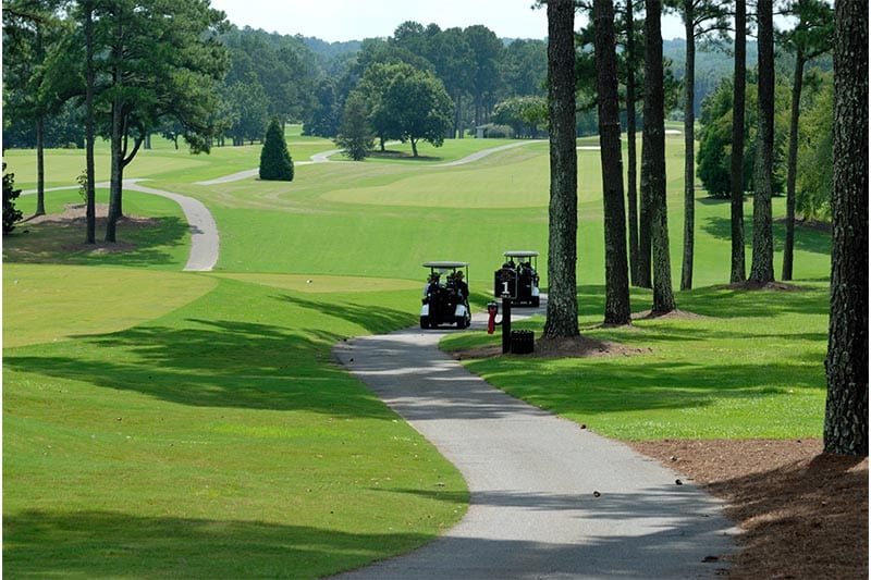 Two golf carts on a path in a wooded part of a golf course.