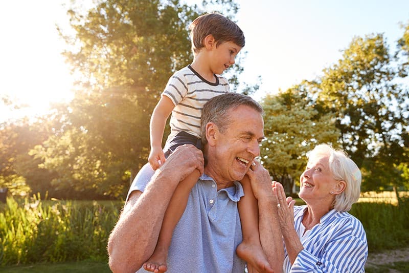 Grandfather giving his grandson a ride on his shoulders in a park in a 55+ community.