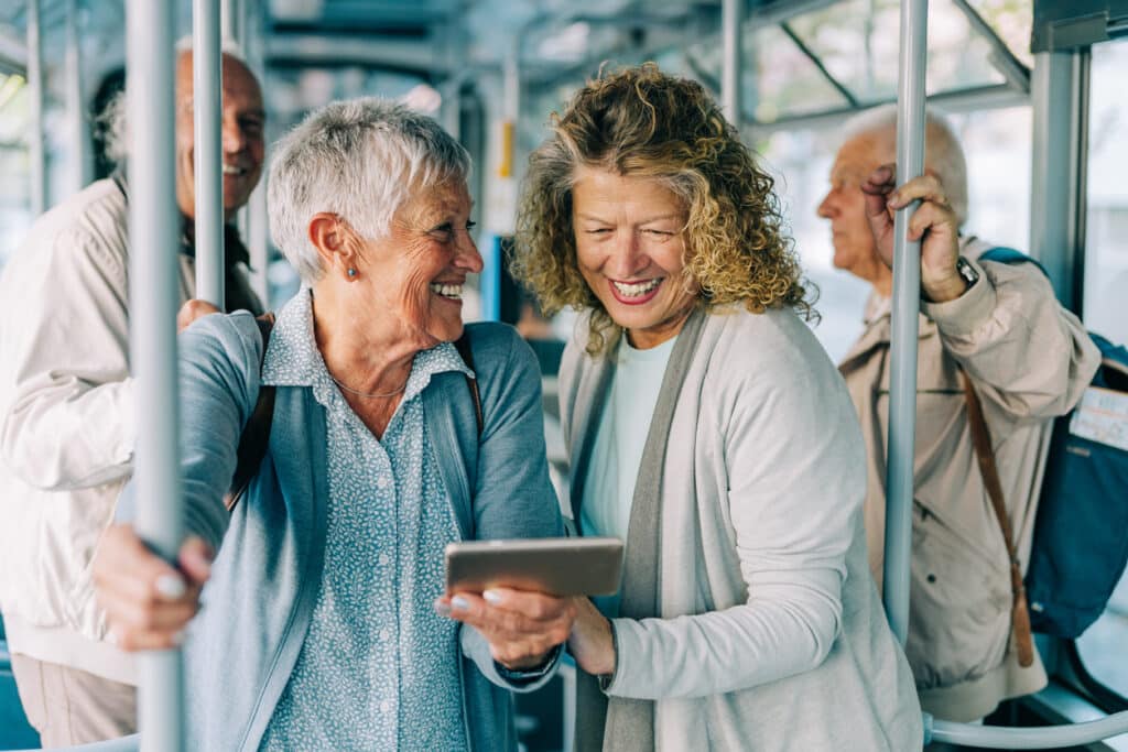 Shot of a two female mature friends using smartphone in public transportation. Two smiling mature couples traveling by bus.