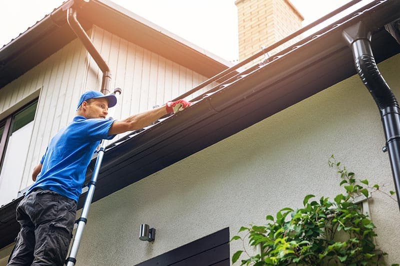 A maintenance worker cleaning the gutters on a home in a 55+ community.