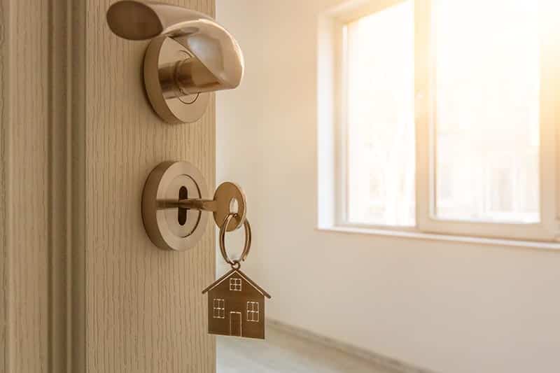 An open door to a new home with a key and a home-shaped keychain.