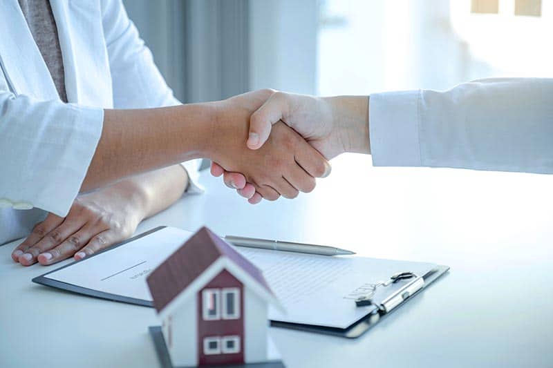 A real estate agent and a buyer shaking hands after closing on a home.