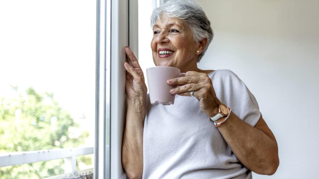 An older woman looks out the window of her home in a retirement community.