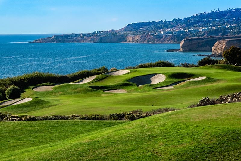 Manicured golf course with sand traps overlooking the Pacific Ocean.