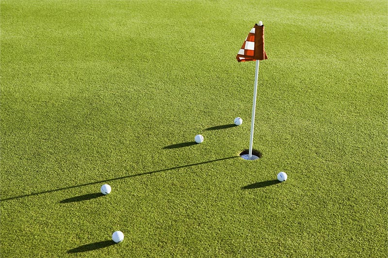 Putting green with flag in hole surrounded by 5 golf balls.