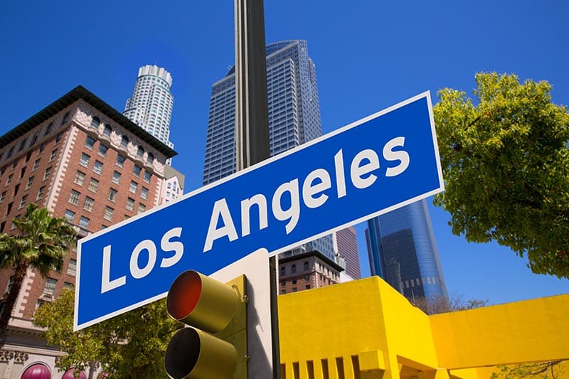 Blue Los Angeles street sign with city buildings in the background.