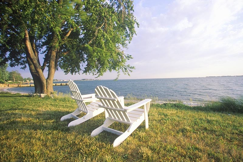 Two white adirondack chairs on a grassy yard overlooking Chesapeake Bay.