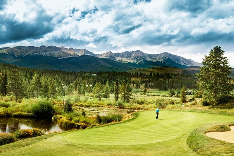 Man on golf course with mountains in the background.
