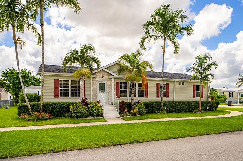 Light yellow manufactured home with green lawn and palm trees in front of the house.