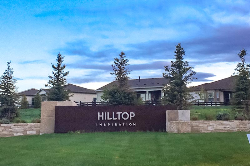 Pine trees behind the community sign at Hilltop at Inspiration in Aurora, Colorado.