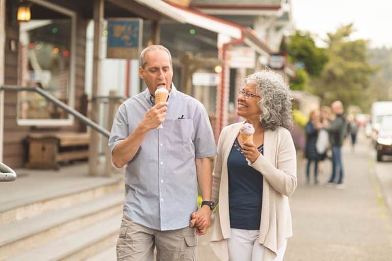 An older couple eats ice cream while walking down the street in their small town retirement community.