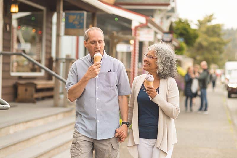 An older couple eats ice cream while walking down the street in their small town retirement community.