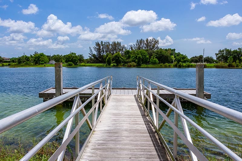 Fishing dock on lake with trees and blue sky.