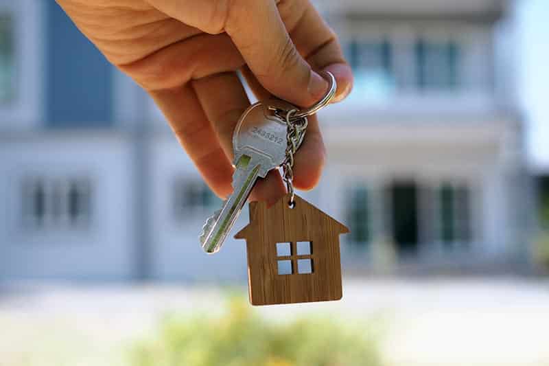 Hand holding key with wooden house key fob attached.