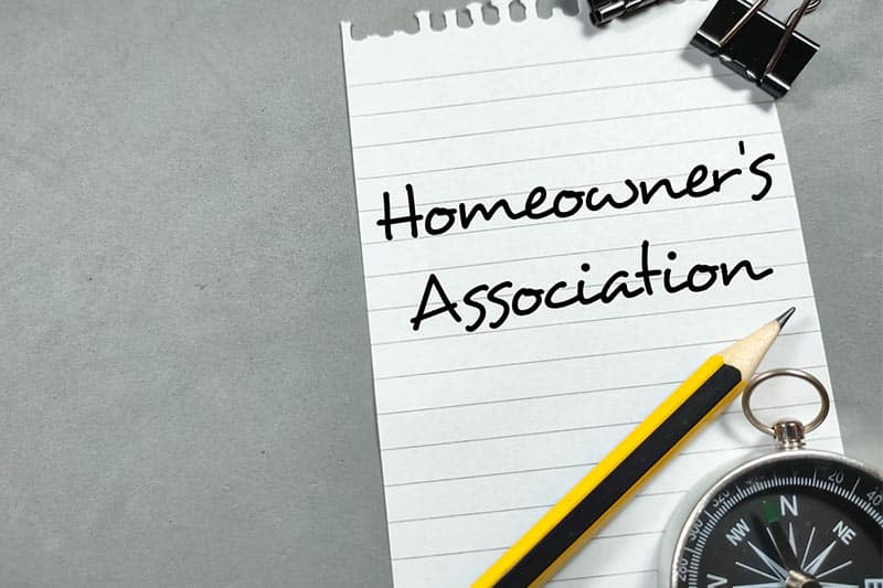 Homeowner’s association written on notepad with clips, pencil, and compass on laying on the paper.