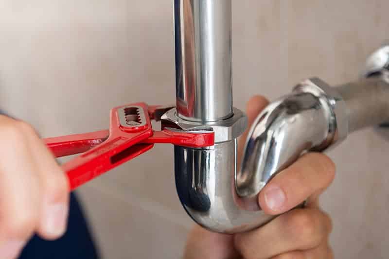 Plumber tightening a joint on kitchen drain.