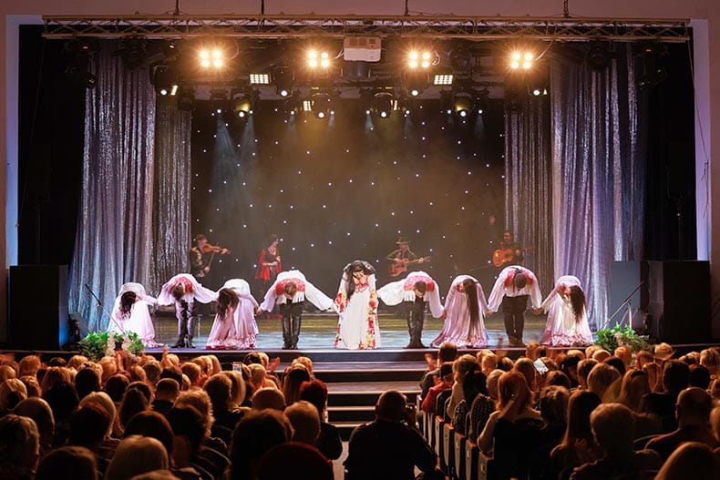 A collective of musicians, singers and dancers in gypsy costumes perform on stage.