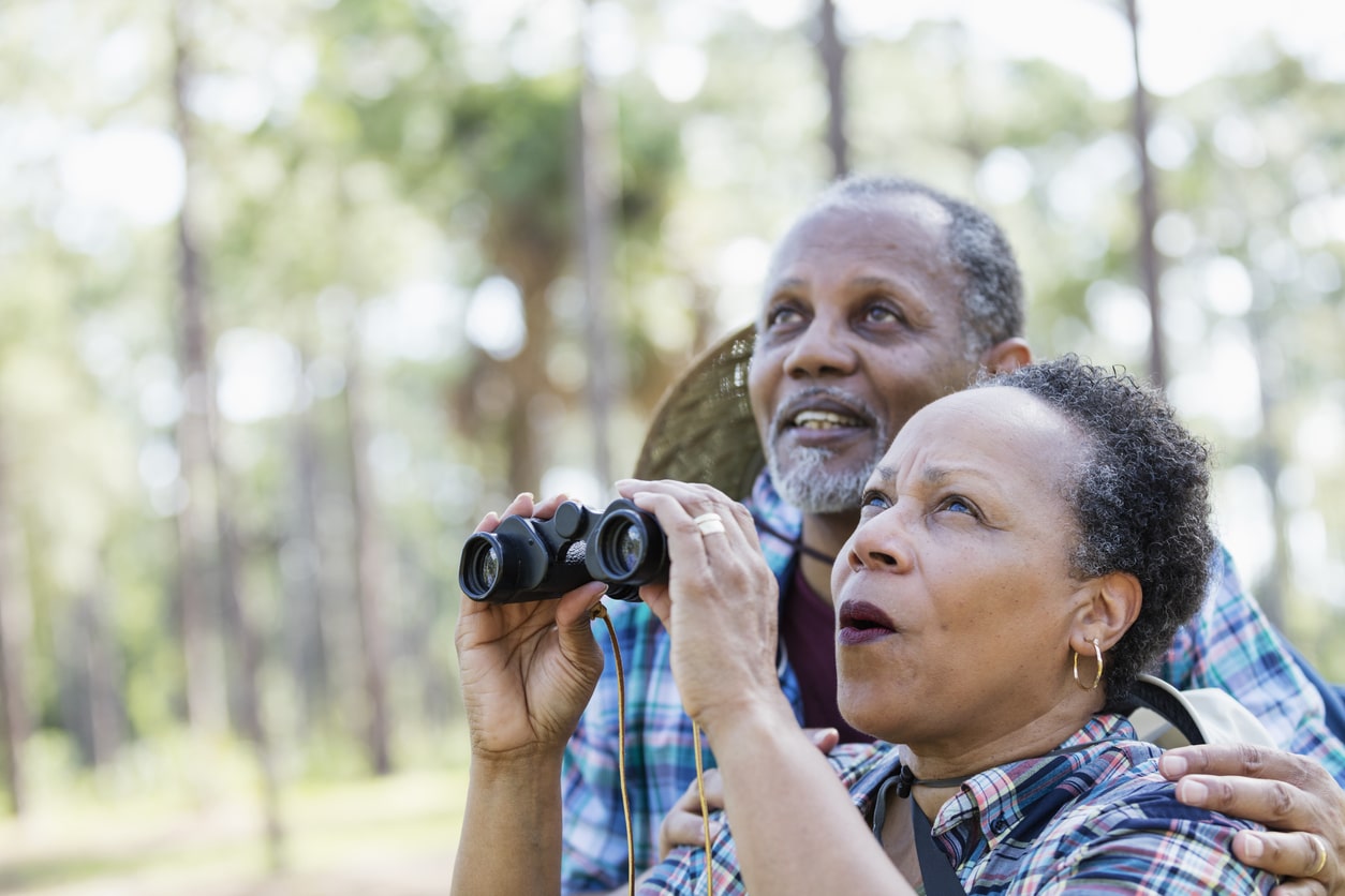 An older couple with binoculars is bird watching, an easy hobby for seniors.