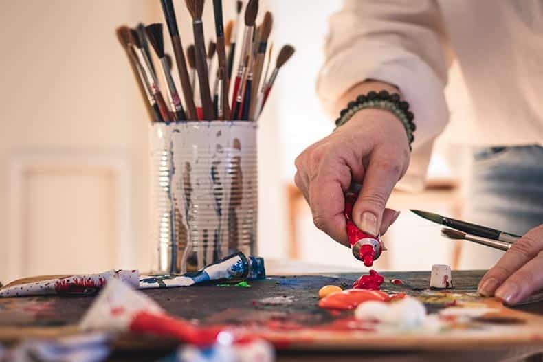 A 55+ woman mixing acrylic colors on a palette for painting in an art studio.