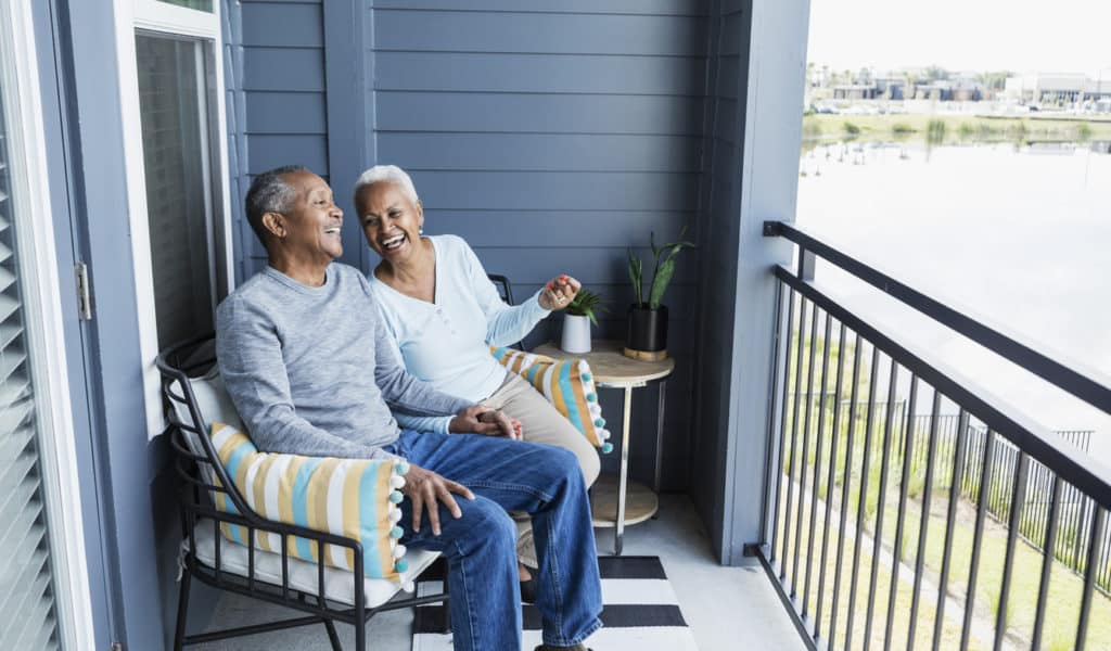 A senior couple sits on the porch of their condo in a 55+ land lease community.