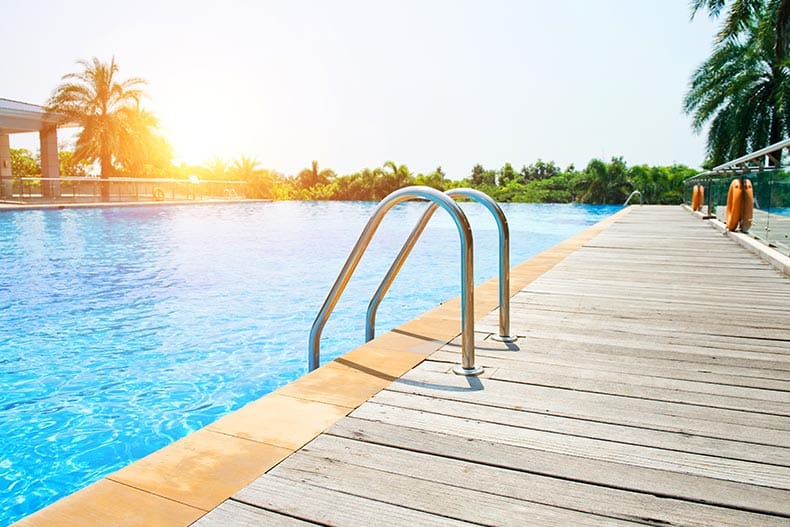 A swimming pool with a ladder and wooden deck at a hotel.