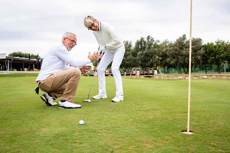 An active adult couple playing golf on the golf course in their 55+ community.