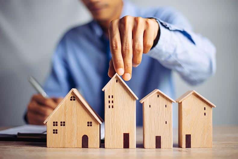 A businessman choosing a mini wood house model on wood table.