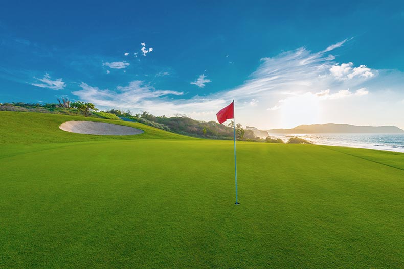 A red flag on a golf course at the ocean side at sunset.