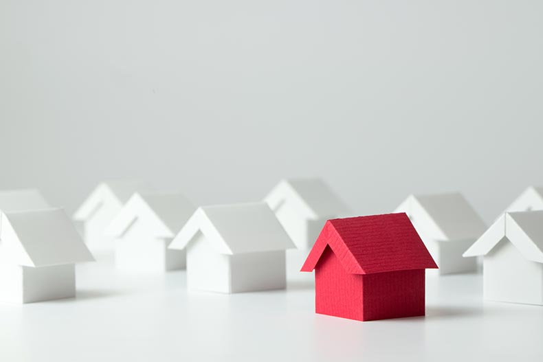 A tiny model red house among white houses.