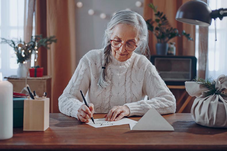 An older woman is a senior pen pal, and she is writing a return letter at her desk.