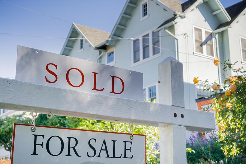 A "Sold" sign in front of a house in a residential neighborhood in California.