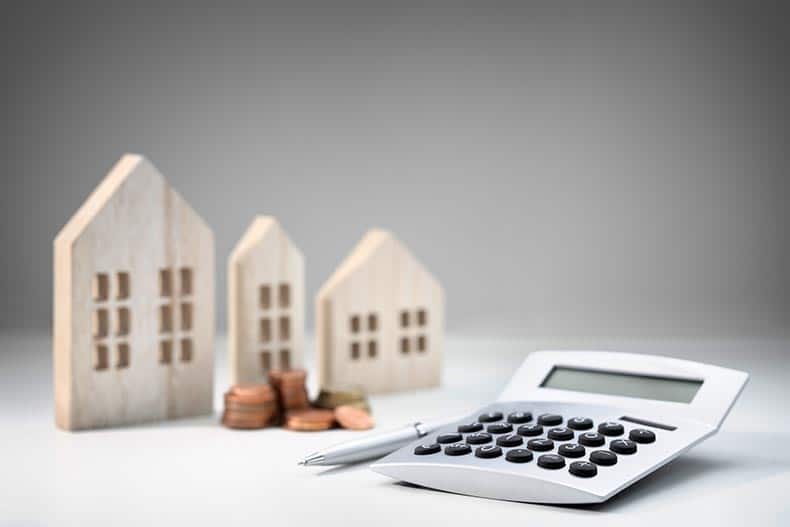 A calculator beside wooden houses and a stack of coins.