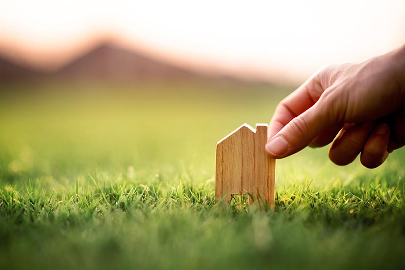 A hand holding a small wooden model home over green grass.