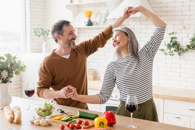 Happy mature couple dancing together in the kitchen at home in a 55+ community.