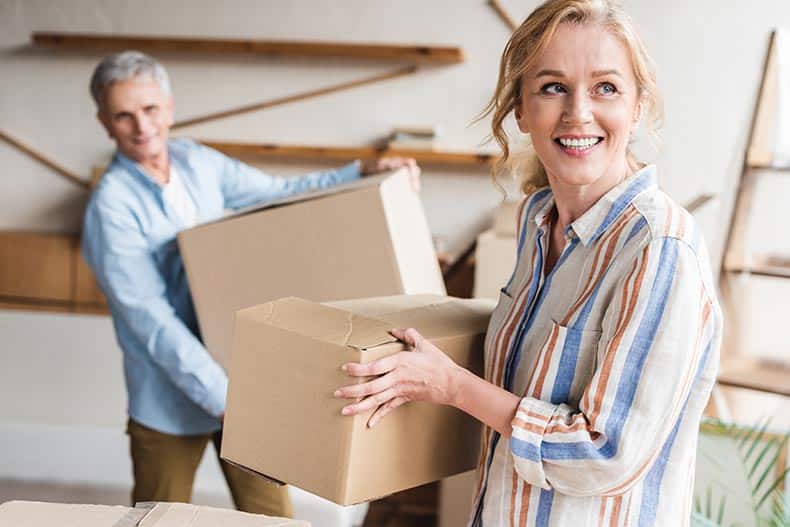 A mature couple carrying cardboard boxes as they downsize their home and move into a 55+ community.