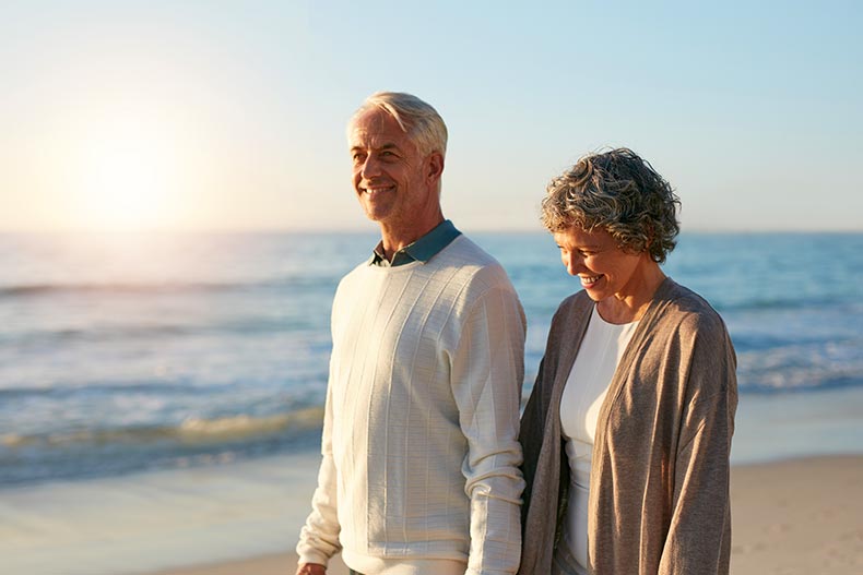 A happy mature couple walking along the beach near their 55+ community.