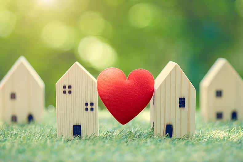 A heart between wooden model houses on grass and green background.