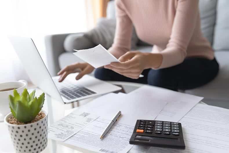 Close up on a woman with a laptop and a calculator working through housing finances.
