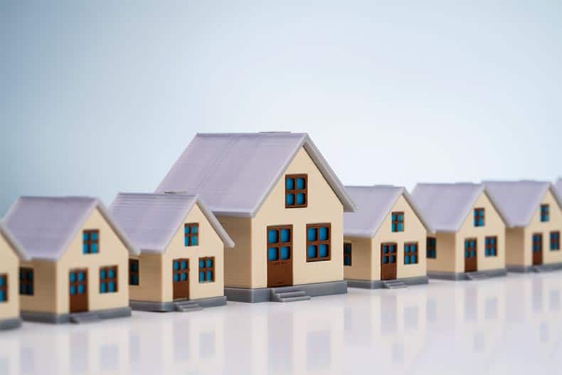 A row of miniature houses on a reflective desk.