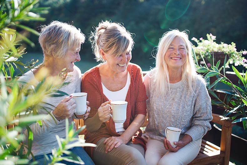 Senior women smiling with coffee while sitting outdoors in their 55+ community.