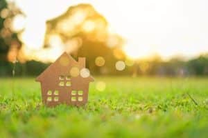 Closed up on a tiny wood home model on green grass with sunlight background.