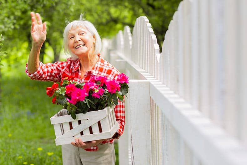 A senior lady waving to her neighbor standing near a fence.